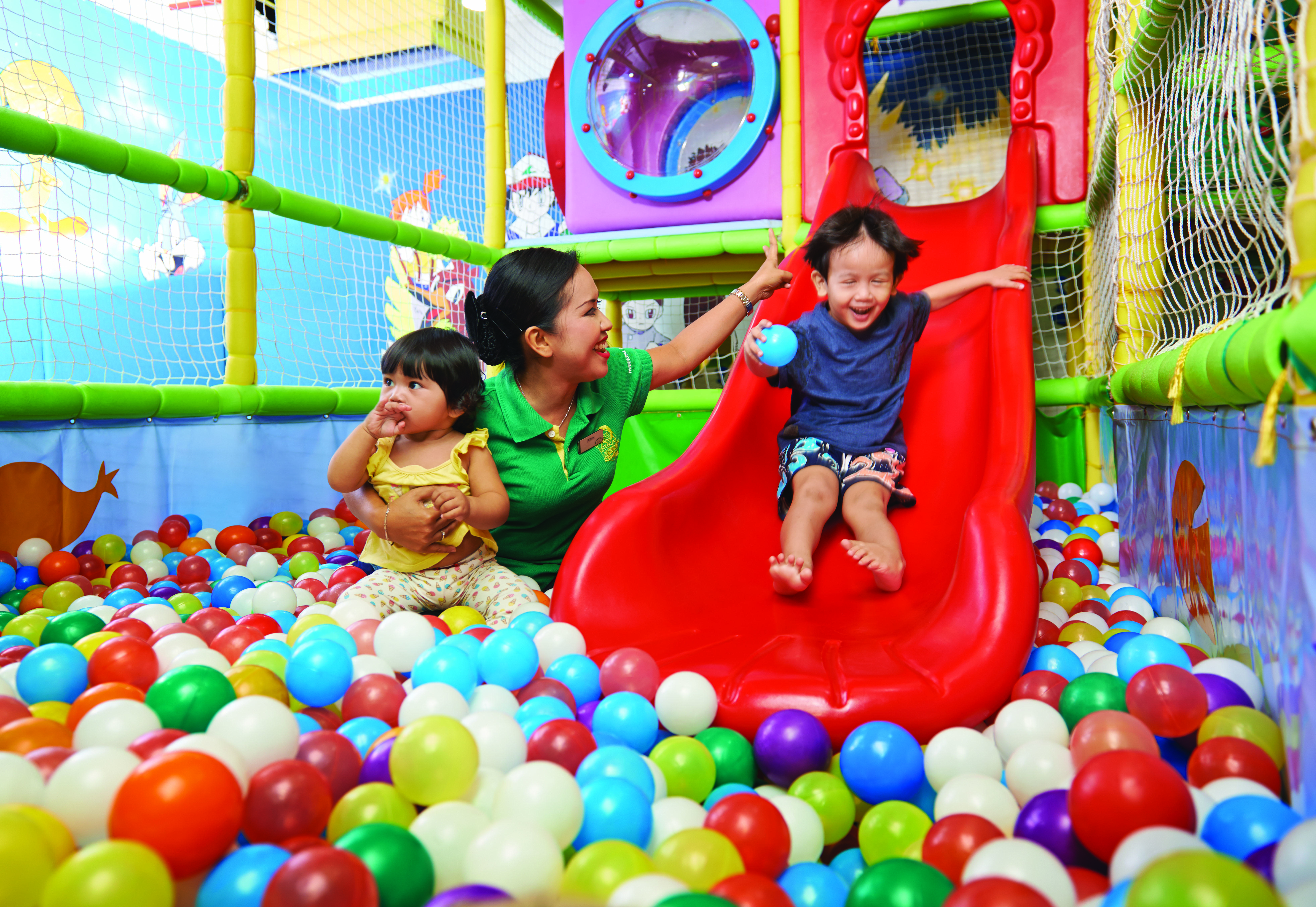 Parkroyal Penang Resort Batu Ferringhi Exterior photo The photo shows a playful indoor environment designed for children. In the center, there is a red slide that a young boy is joyfully sliding down. He appears to be having fun, smiling as he descends. Nearby, a woman is attentively engaging with him, 