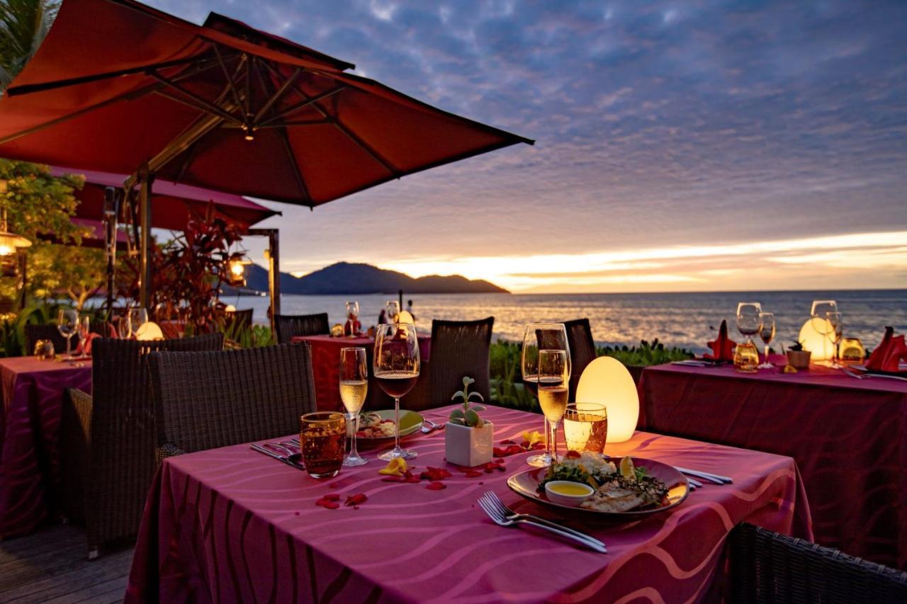 Parkroyal Penang Resort Batu Ferringhi Exterior photo The photo shows a beautiful outdoor dining setup at a restaurant during sunset. The tables are adorned with pink tablecloths and are set with dishes and glasses. There are decorative elements like flowers, and the setting includes umbrellas to provid