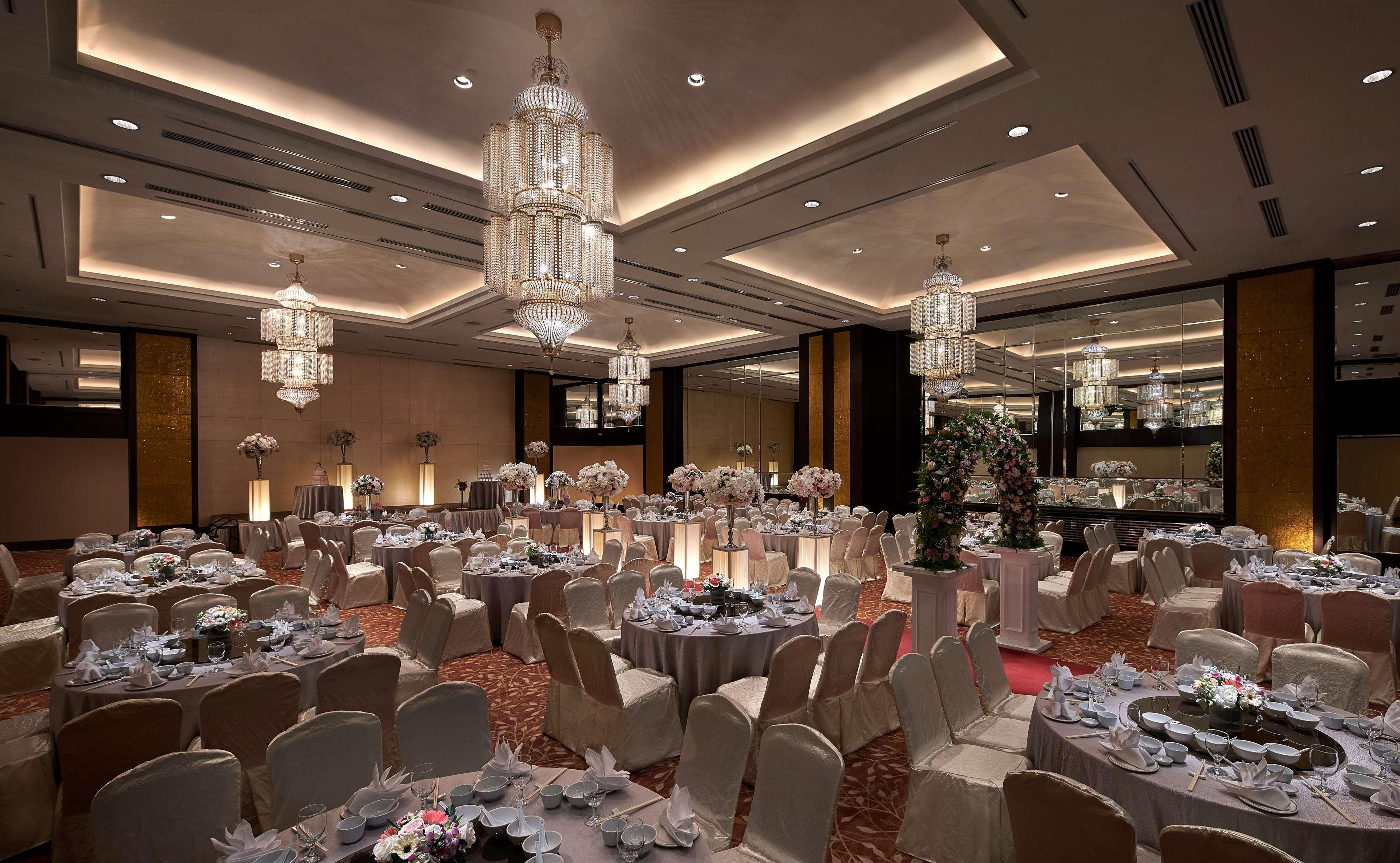 Parkroyal Penang Resort Batu Ferringhi Exterior photo The photo shows an elegantly decorated banquet hall. There are multiple round tables arranged throughout the space, each covered with light-colored tablecloths and set with white dinnerware. The tables are adorned with floral centerpieces, adding a t