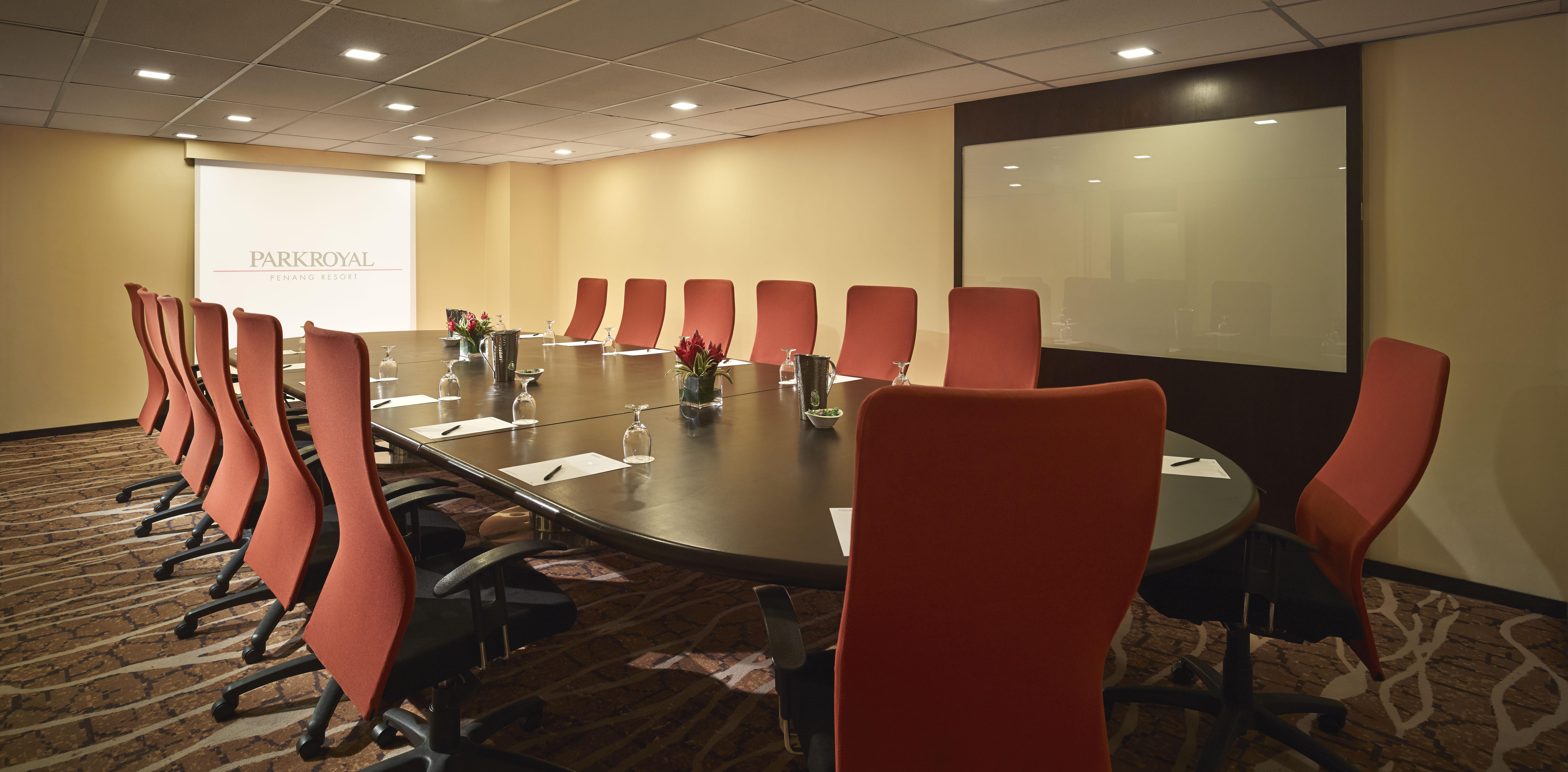 Parkroyal Penang Resort Batu Ferringhi Exterior photo The photo shows a conference room with a large, oval-shaped table surrounded by several orange chairs. The room is well-lit, featuring neutral-colored walls and a modern design. In the center of the table, there are small potted plants, and water gla