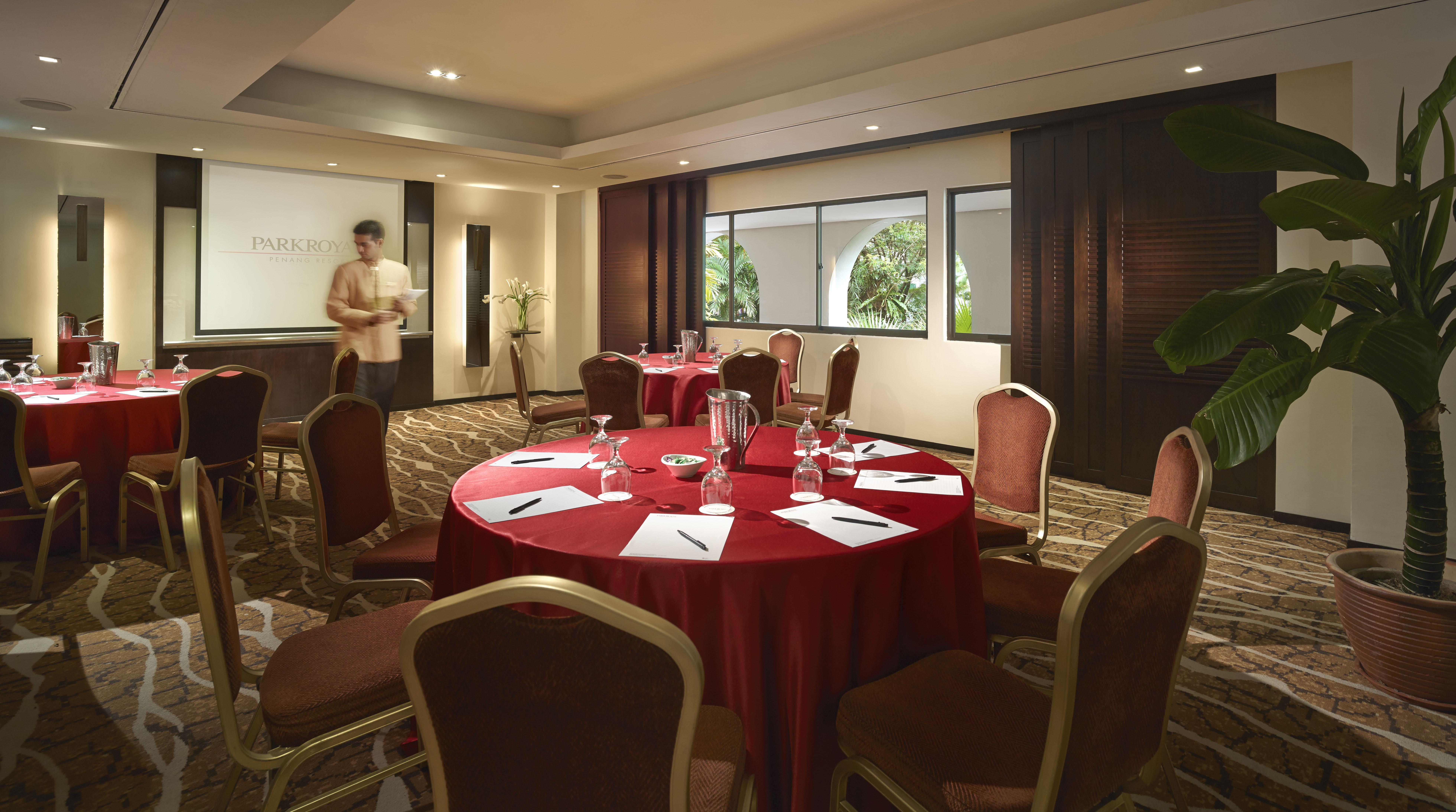 Parkroyal Penang Resort Batu Ferringhi Exterior photo The photo shows a conference or meeting room featuring a round table dressed in a red tablecloth. The table is set up with several place settings that include white notepads and pens. Surrounding the table are chairs with a gold frame. In the backgro